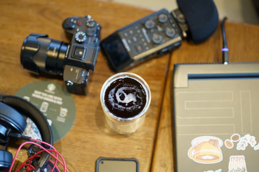 Overhead view of a workspace featuring a camera, headphones, audio gear, and a cup of coffee.