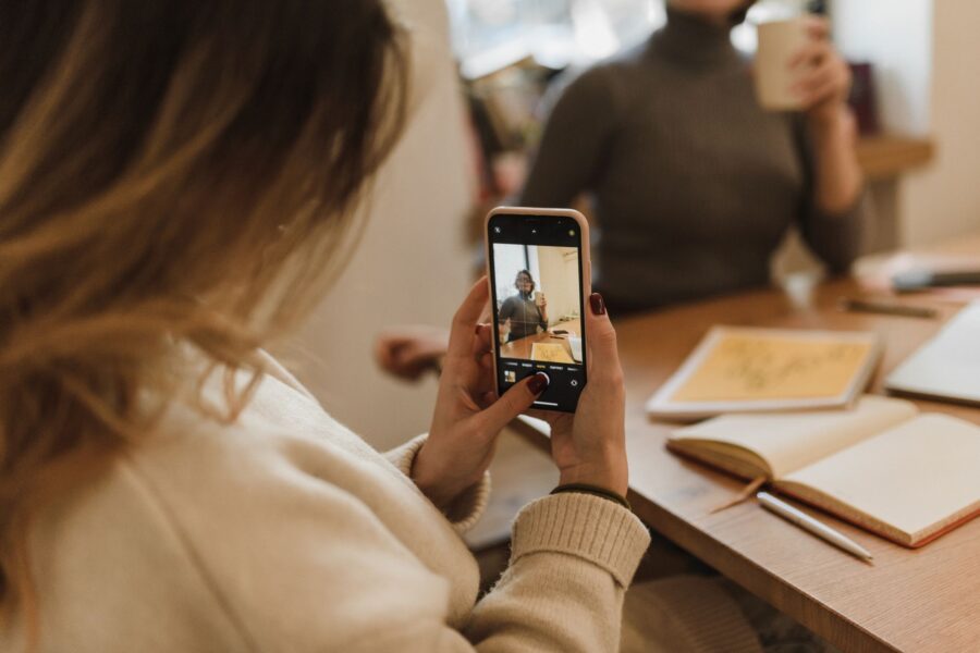 Woman captures a relaxed office moment with smartphone, emphasizing social media and small business.